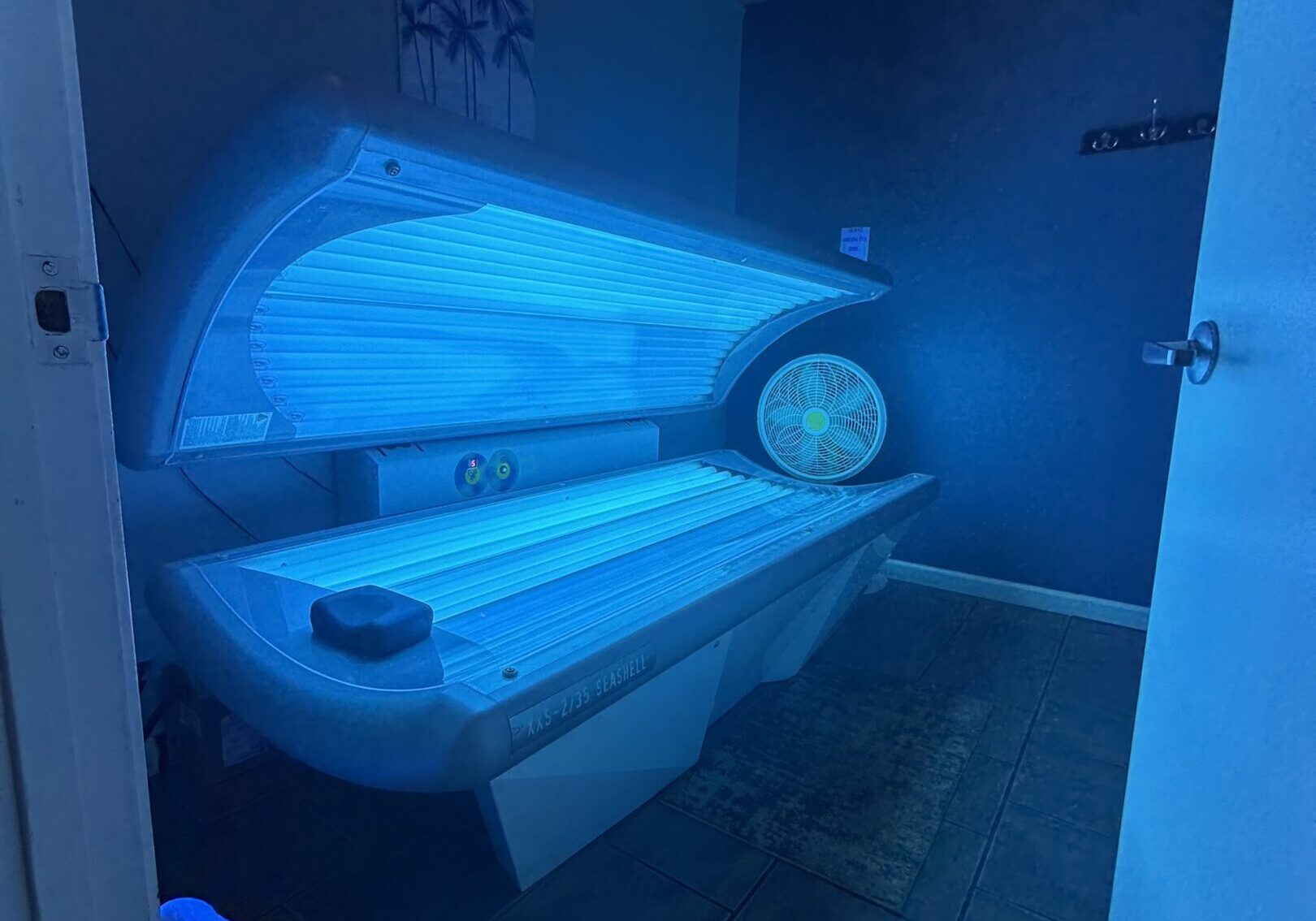 An open tanning bed glowing blue in a dimly lit room.