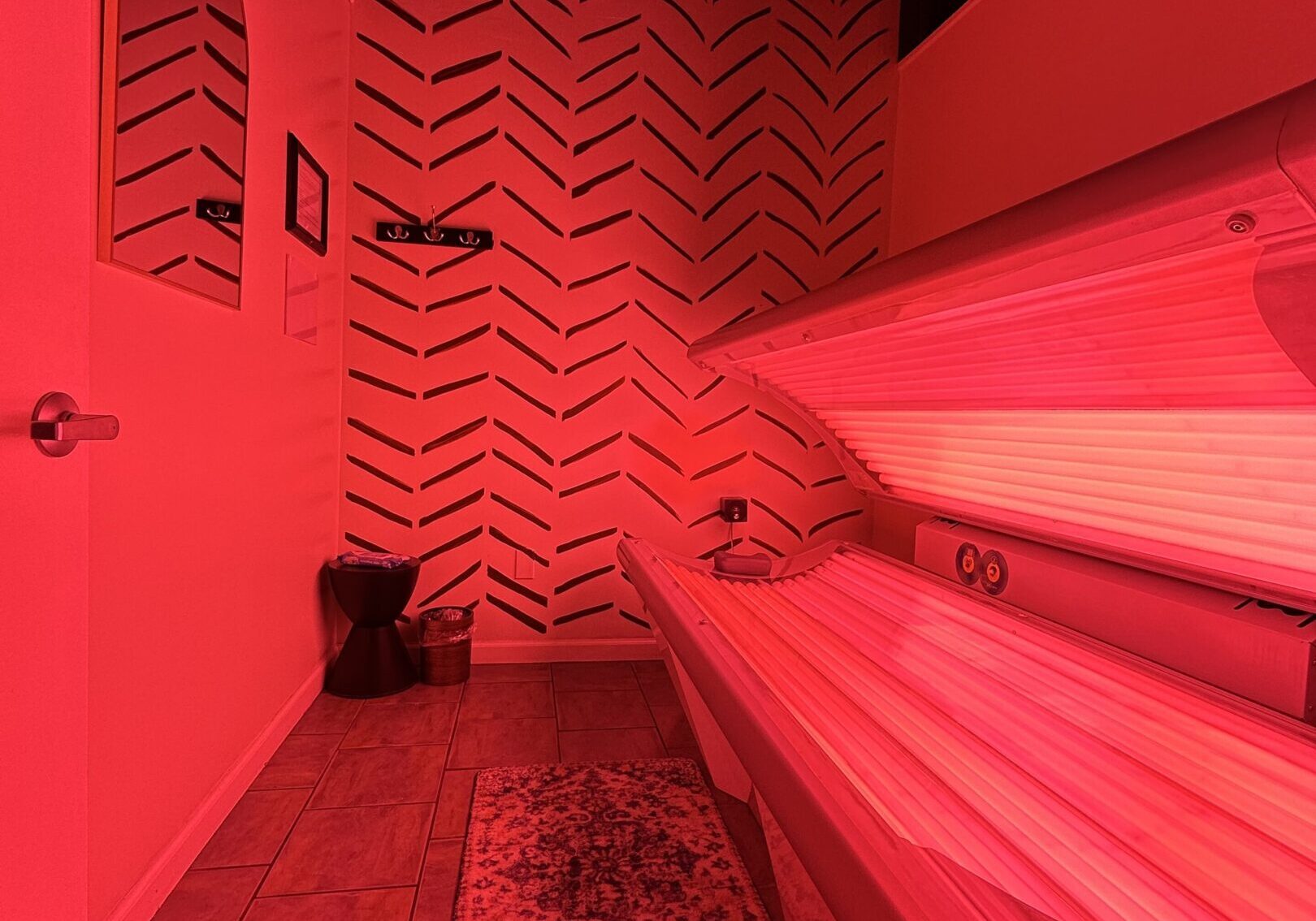 Red-lit tanning bed in a modern room with patterned walls.